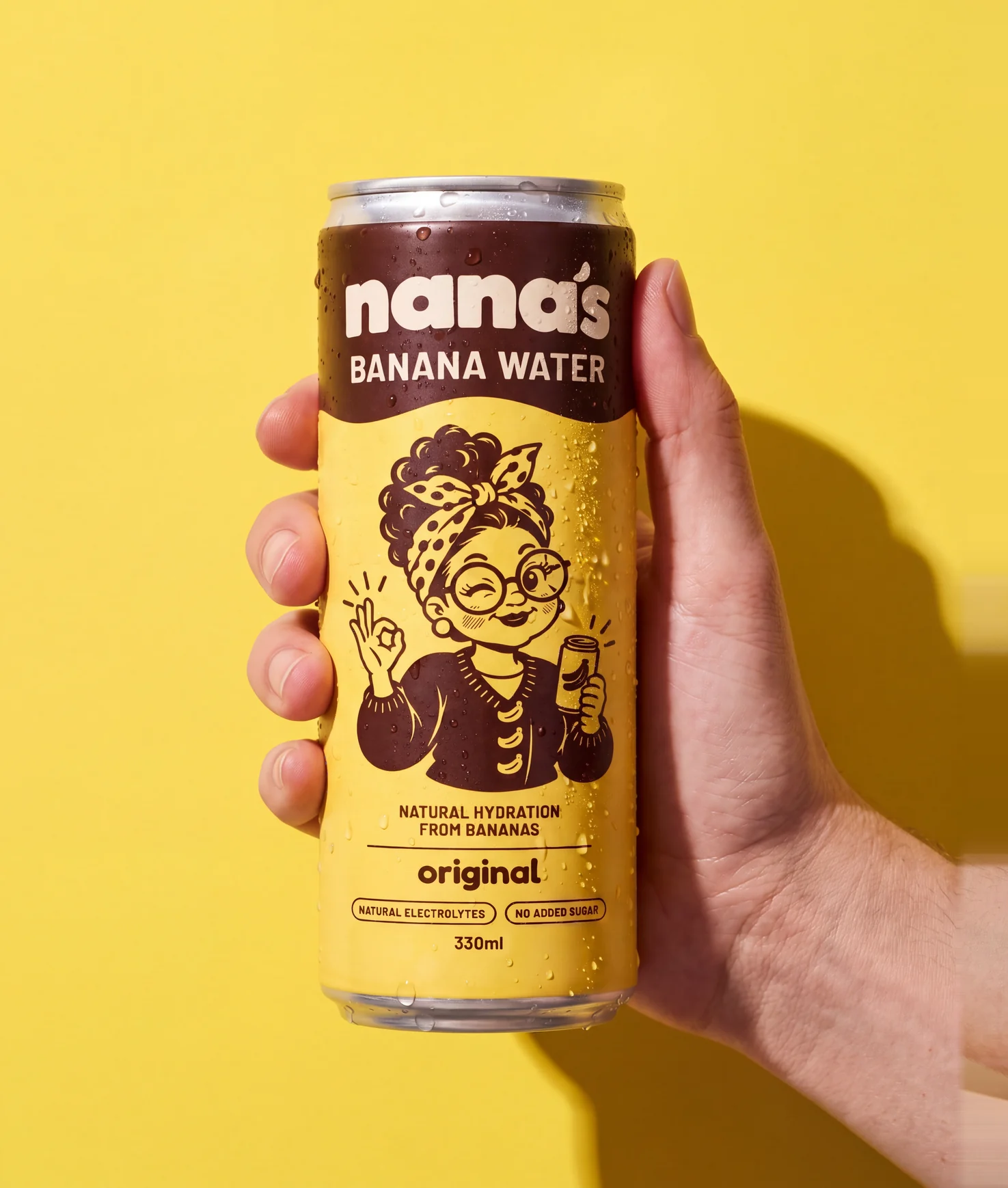 A hand holding a cold can of Nana's Original banana water against a yellow wall